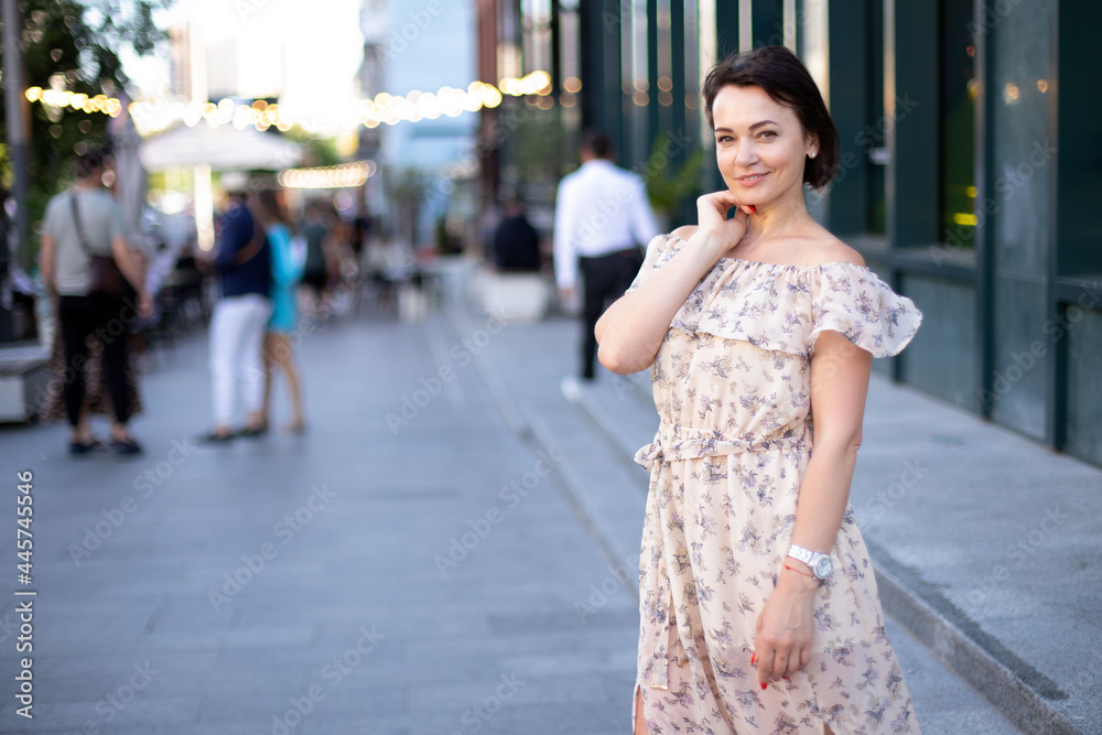 an adult contented woman in a dress stands in the middle of an urban street against the backdrop of lanterns. place for your design an adult contented woman in a dress stands in the middle of an urban street against the backdrop of lanterns. place for your design