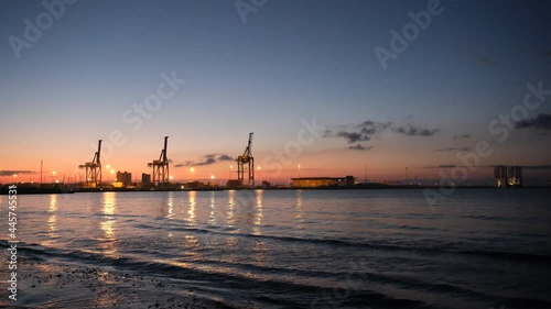 Time-lapse of the cranes in the port with the sea and clouds in the background