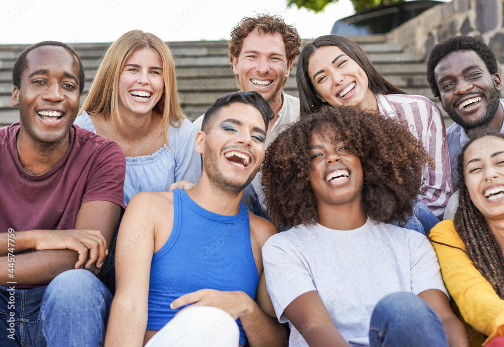Fototapeta premium Group of mutliracial friends smiling on camera while sitting in the city - Millennial people enjoy time together outdoor - Diversity, friendship and happiness concept