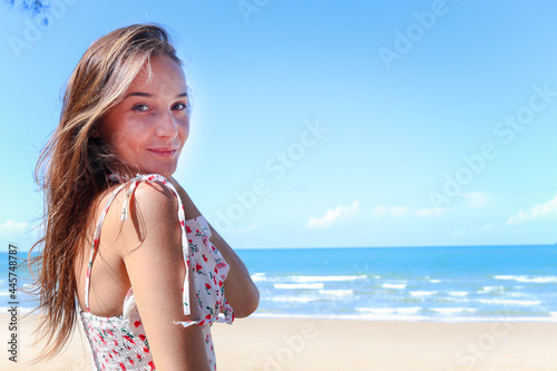 Portrait of smiling young beautiful woman with blond long hair standing on tropical blue sea summer beach, relaxing vacation summer concept.