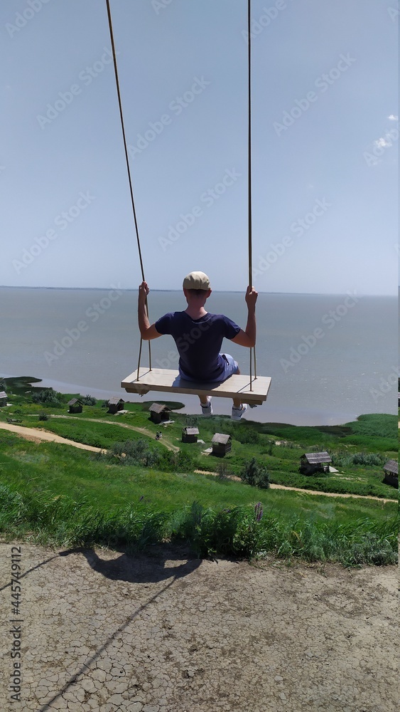 Guy rides on a swing overlooking the sea Guy rides on a swing overlooking the sea