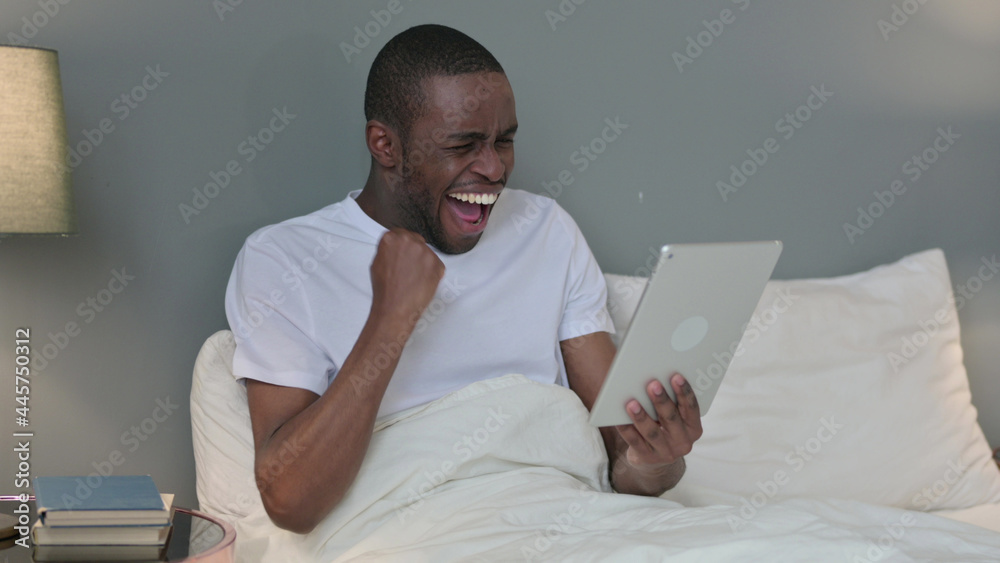 Excited Young African Man Celebrating on Tablet in Bed Excited Young African Man Celebrating on Tablet in Bed