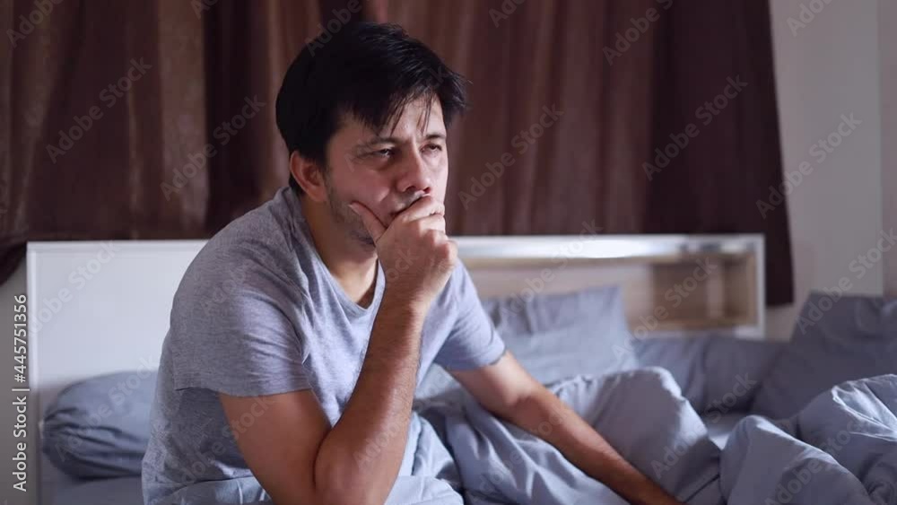 Asian man sitting in bed thinking about life's problems, depressed and strain