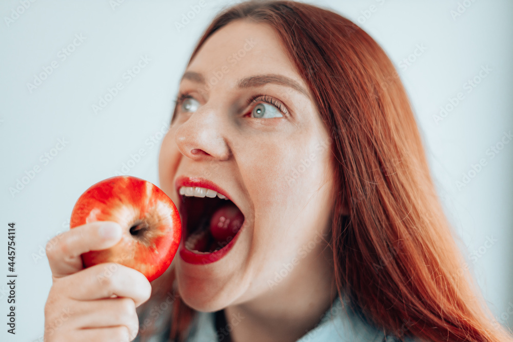 Portrait of cheerful young girl eating red apple on gray wall background. Woman biting ripe fruit. Apple vitamin snack. Portrait of cheerful young girl eating red apple on gray wall background. Woman biting ripe fruit. Apple vitamin snack.