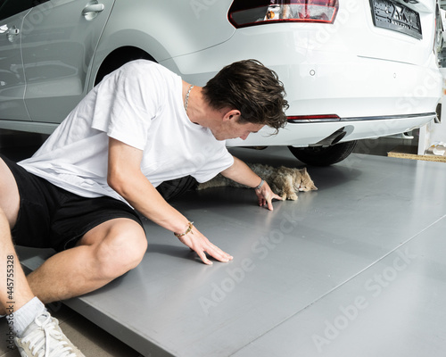 young man stroking a cat. A cat lying in a new car shade.