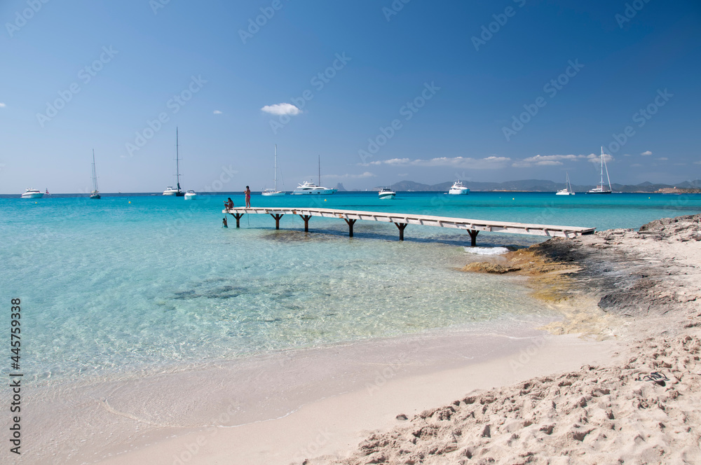 A couple of tourists watch the horizon over the Mediterranean Sea from a wooden pier on a beach in Formentera, Spain