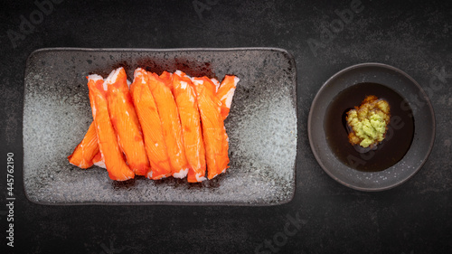 imitation Alaska crab sticks with Wasabi and Shoyu soy sauce in ceramic plate on dark tone texture background, top view