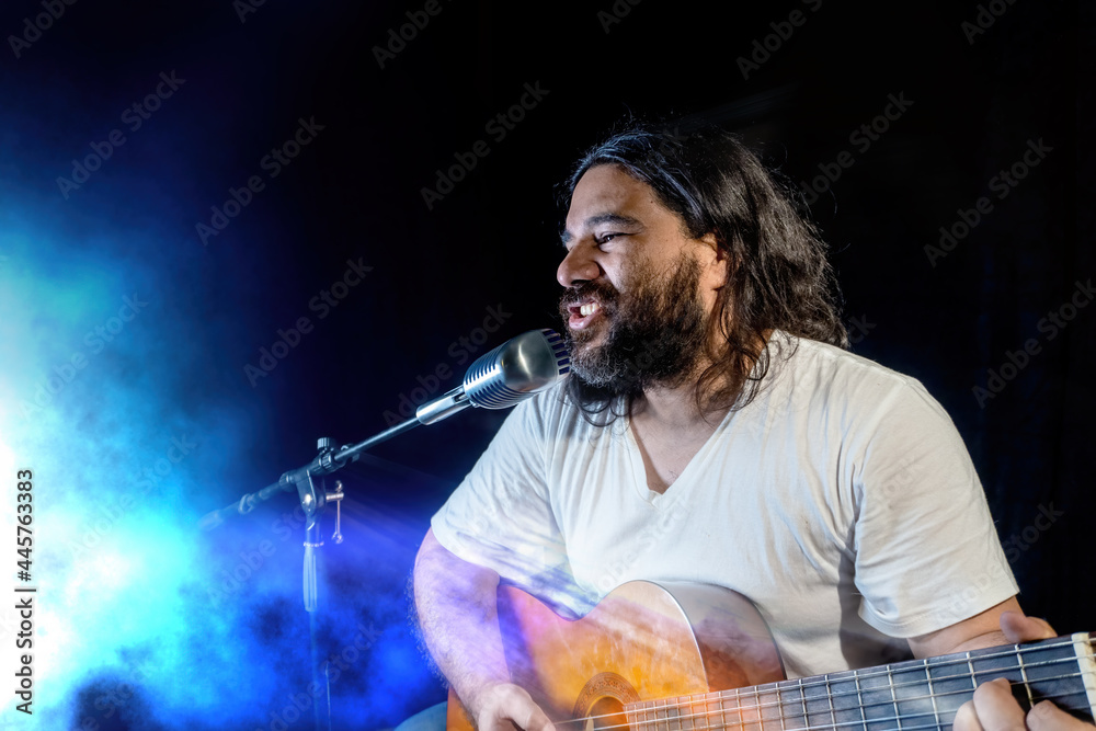 Obraz premium A young Hispanic man singing passionately and playing the guitar at a concert
