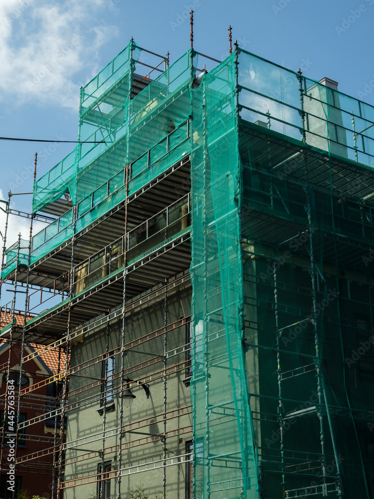 building with scaffolding and green mesh on sunny day