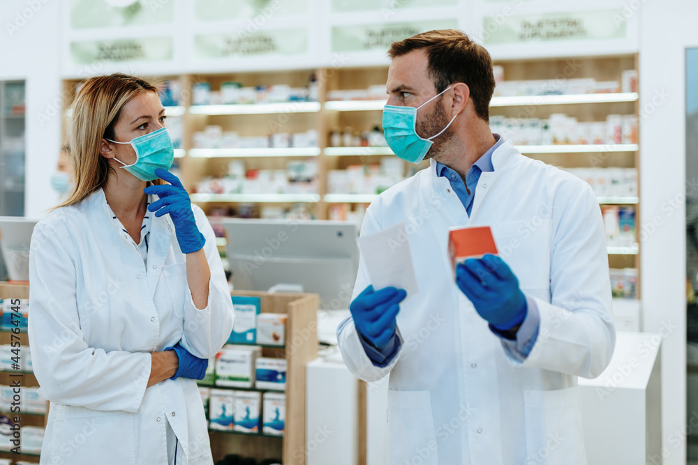 Obraz premium Male and female pharmacists with protective mask on their faces working at pharmacy. Medical healthcare concept.