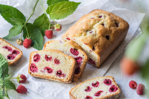 Homemade raspberry loaf cake on parchment paper with fresh raspberries on branches on grey background, selective focus