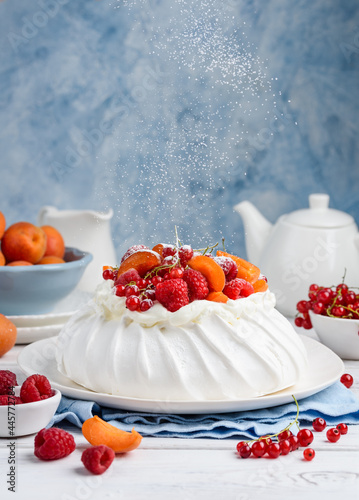 Homemade Pavlova cake with fresh raspberries, red currants and apricots. Flying powdered sugar. Selective focus 