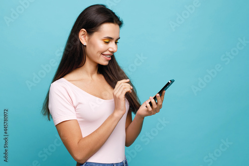 Pretty girl with smartphone in hands addicted to social media. Portrait of smiling young woman browsing on telephone. Female expresses joyful emotions.