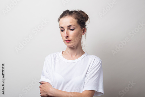 Young woman in a white shirt looks into the bottom on a light background