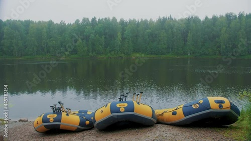 Slow motion. Front view of boats for rafting, kayaking, canoes, kayaks are standing on the river bank, against the background of a dense green forest. A wide, fast river, cloudy weather.
