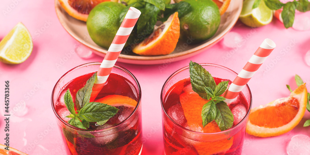 Refreshing summer red cocktail in glasses with blood orange and lime on pink background with mint Refreshing summer red cocktail in glasses with blood orange and lime on pink background with mint