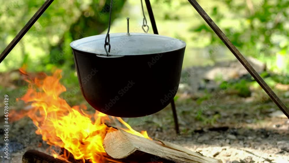 Tourists prepare lunch in hiking pot on campfire at campsite. Bowler on bonfire. Tourists prepare lunch in hiking pot on campfire at campsite. Bowler on bonfire.