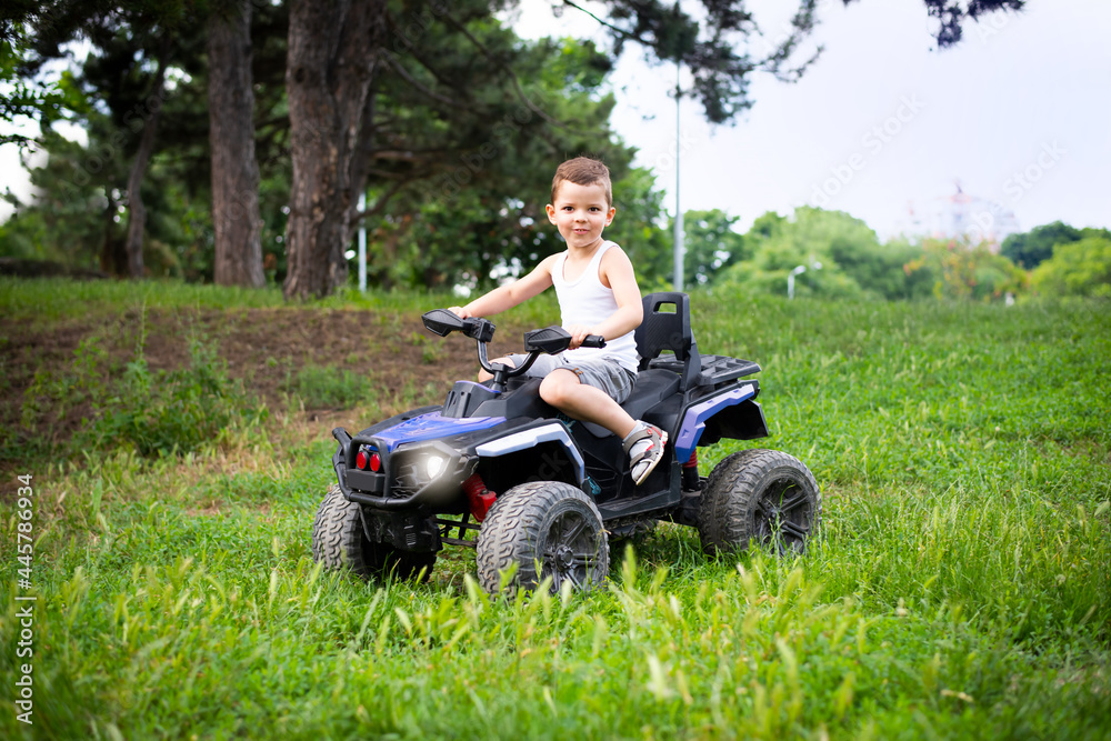 Fototapeta premium A cute five year old boy rides a black and purple ATV Quad bike in a summer park.