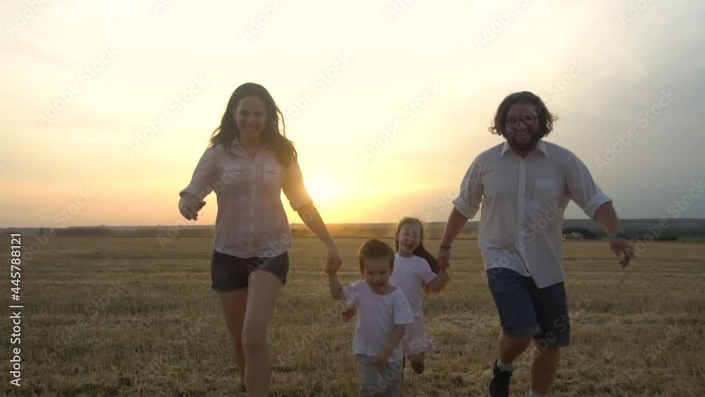 Mom, dad, son and daughter run holding hands in the park.Parents and cheerful children.Slow motion. Mom, dad, son and daughter run holding hands in the park.Parents and cheerful children.Slow motion.
