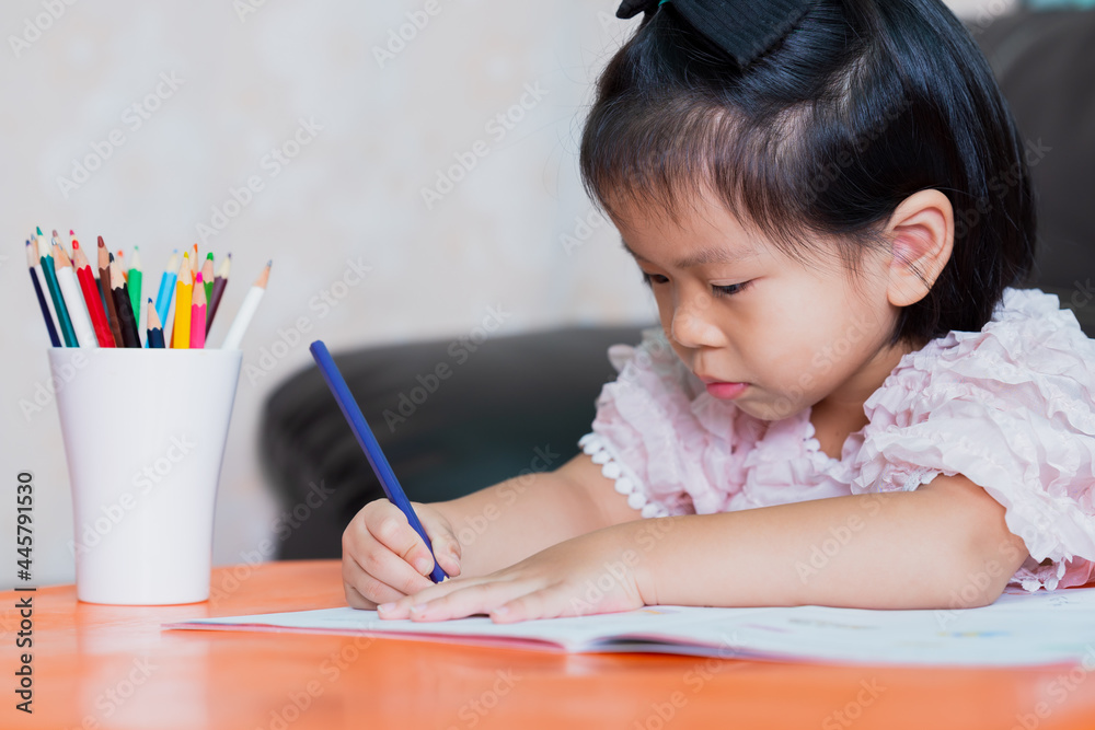 Portrait of Asian pupil girl doing homework at home. Child holding color pencil with right-hand. Kid painting on paper book. Portrait of Asian pupil girl doing homework at home. Child holding color pencil with right-hand. Kid painting on paper book.