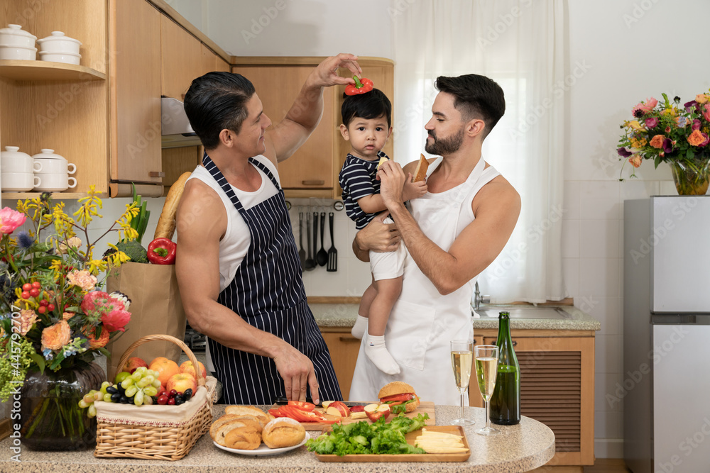 Gay couple feeding food their adopted child together at kitchen