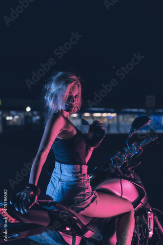 portrait of a girl in the rays of neon light on a motorbike at night in an empty parking lot