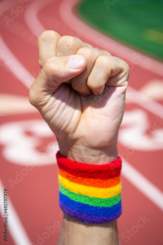 Athlete wearing gay pride rainbow wristband punches the air in front of a sports track background