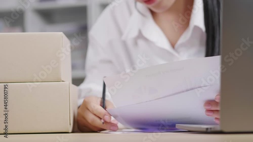 Close up hand woman checking stock, taking a note and typing on  laptop at home to key document, online sales channel, woking at home, putting boxes on the table