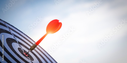 Close up shot red darts arrows in the target of dartboard center on dark blue sky background. Business target or goal success and winner concept.