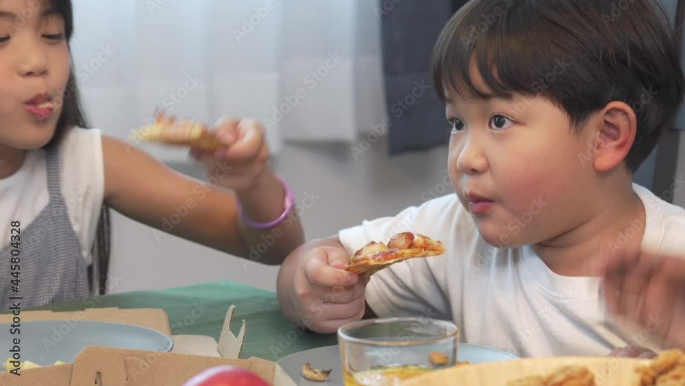 Happy Asian family parents with little daughter and son eating fried chicken and pizza for dinner together. Father and mother with child boy and girl enjoy eating and sharing a meal together at home. Happy Asian family parents with little daughter and son eating fried chicken and pizza for dinner together. Father and mother with child boy and girl enjoy eating and sharing a meal together at home.