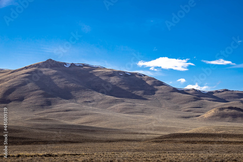 A mountain standing in front of a rugged prairie with brilliant blue skies with clouds in Idaho.