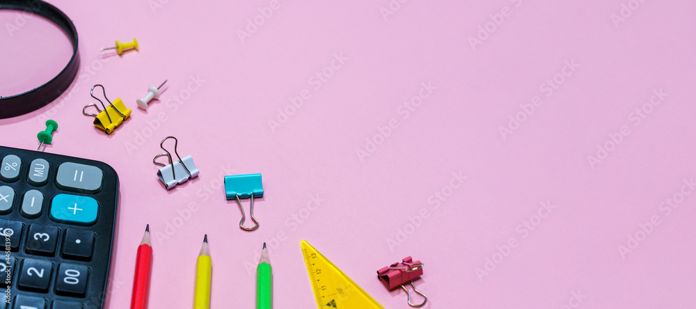 Various office supplies on a pink background. Back to school concept. Calculator and magnifier with pencils of different colors, top view