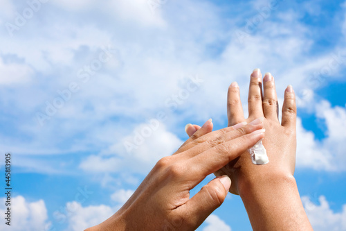 Hand of female holding sunscreen. Very sun light Sky background.Health concepts and skin care