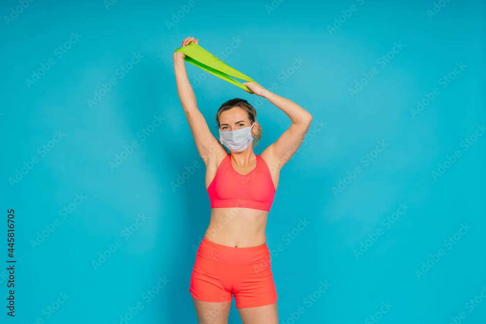 Fototapeta premium Woman in face protection mask and fitness wear isolated over blue background.
