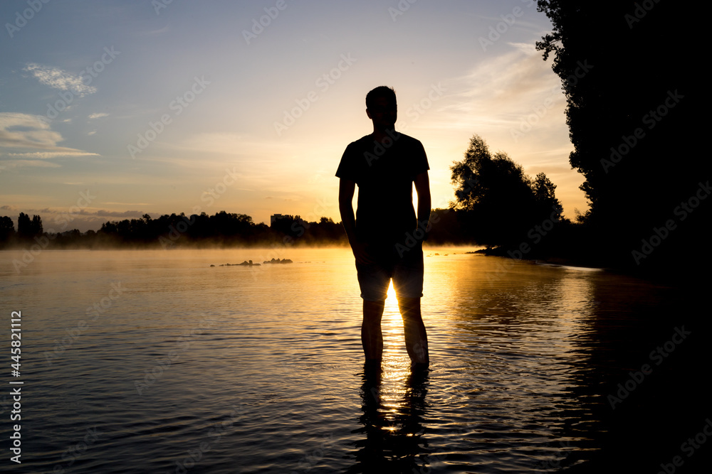 Junger Mann im Sonnenaufgang am Flußufer