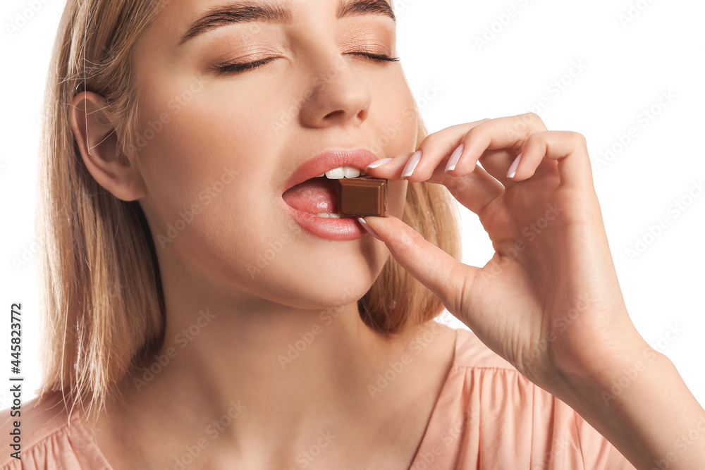 Beautiful young woman eating tasty chocolate on white background Beautiful young woman eating tasty chocolate on white background