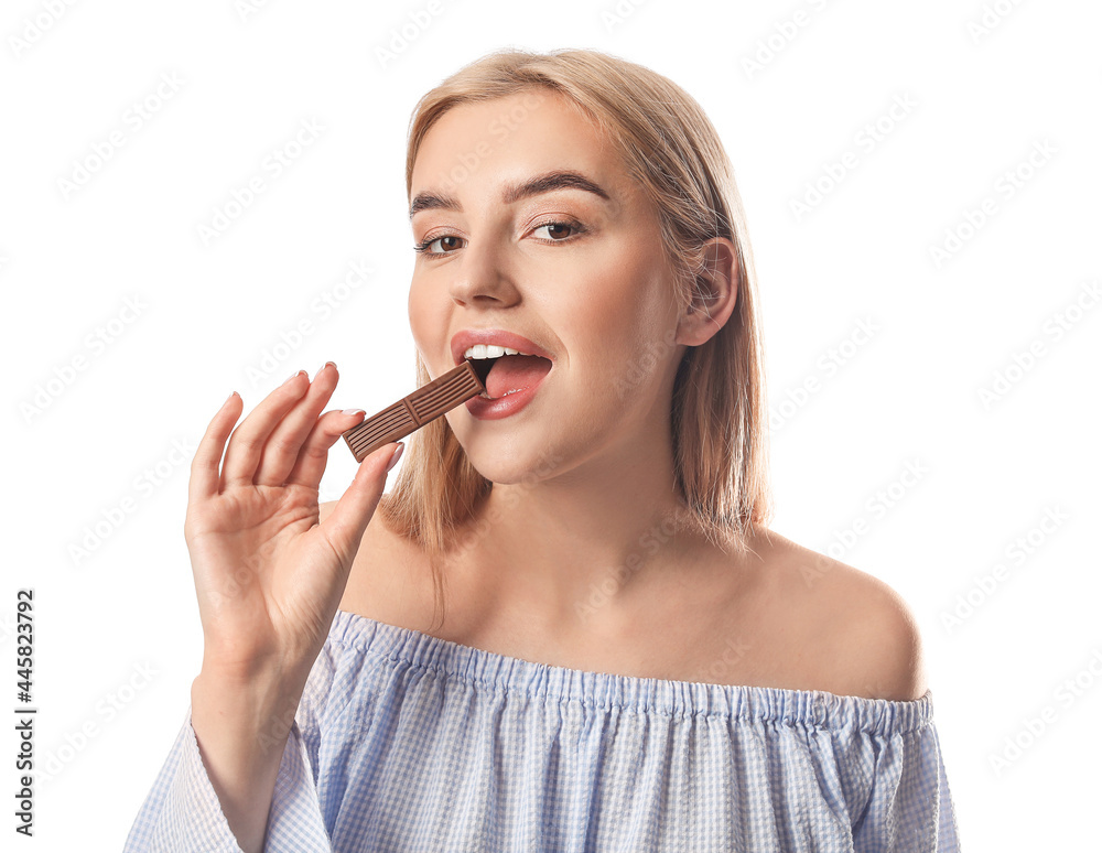 Beautiful young woman eating tasty chocolate on white background