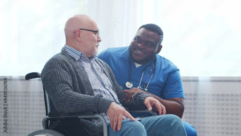 African-American caregiver and old disabled man in a wheelchair. Professional nurse and handicapped patient in a nursing home. Assistance, rehabilitation and health care. African-American caregiver and old disabled man in a wheelchair. Professional nurse and handicapped patient in a nursing home. Assistance, rehabilitation and health care.