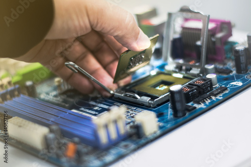 A young man is using his hand to pick up a PC computer CPU on a motherboard with many zips to upgrade a new CPU.