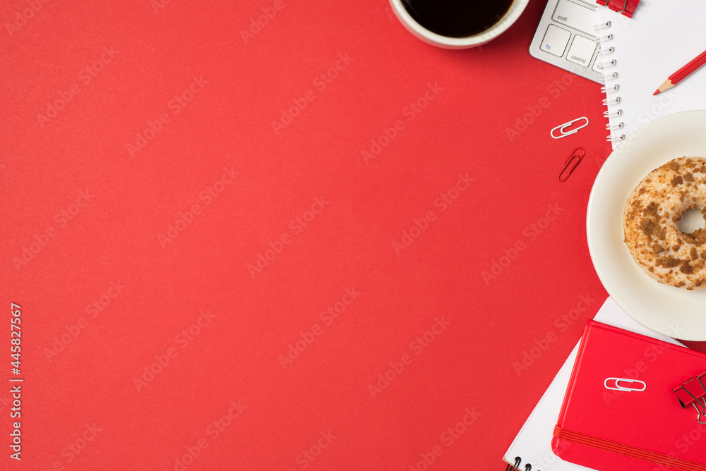 Top view photo of workplace keyboard clips red pencil red copybooks cup of coffee and plate with decorated glazed donut on isolated red background with copyspace Top view photo of workplace keyboard clips red pencil red copybooks cup of coffee and plate with decorated glazed donut on isolated red background with copyspace