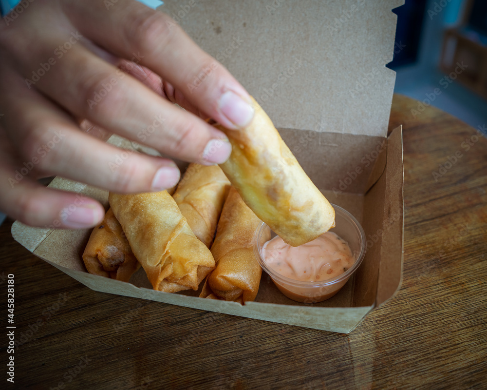 Fried spring rolls in a brown takeaway container with creamy sauce.