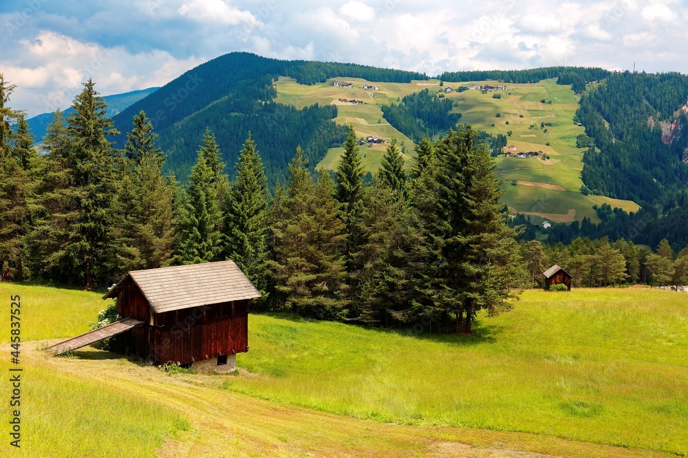 Summer scenery of beautiful Dolomites with Giogo Grande on the mountainside in background and wooden barns on green grassy hills in San Martino in Badia, Bolzano, South Tyrol, Italy, Europe