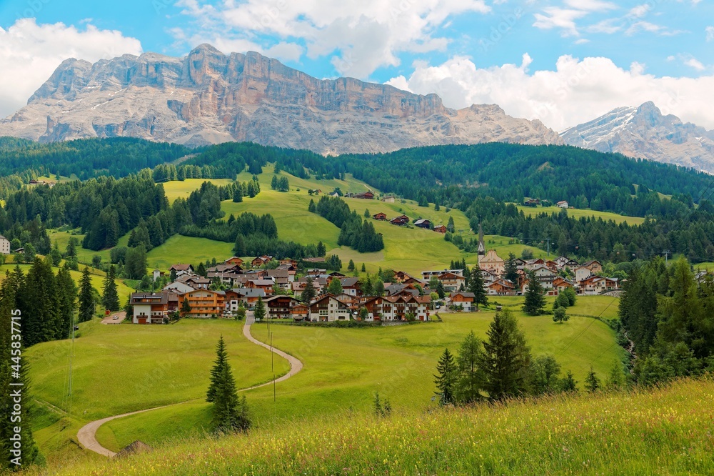 Summer scenery of a beautiful village at foothills of rugged Sasso di Santa Croce & a country road winding in the green grassy valley in Val Badia, Alta Badia, Dolomiti, Trentino, South Tyrol, Italy