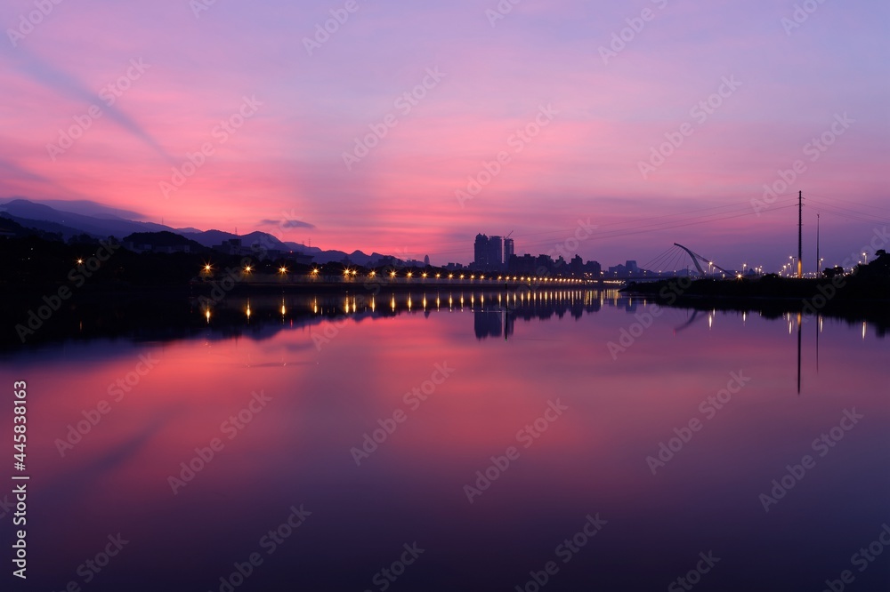 Beautiful Keelung River in morning twilight, with cable-stayed Dazhi Bridge in background and riverside street lamp lights under dramatic dawning sky reflected in peaceful water in Taipei City,Taiwan