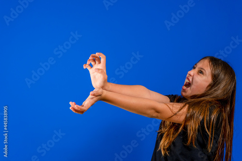 Pretty preteen girl throwing an imaginary kame kame ha with a lot of anger to win the fight isolated on blue studio background. Fun concept