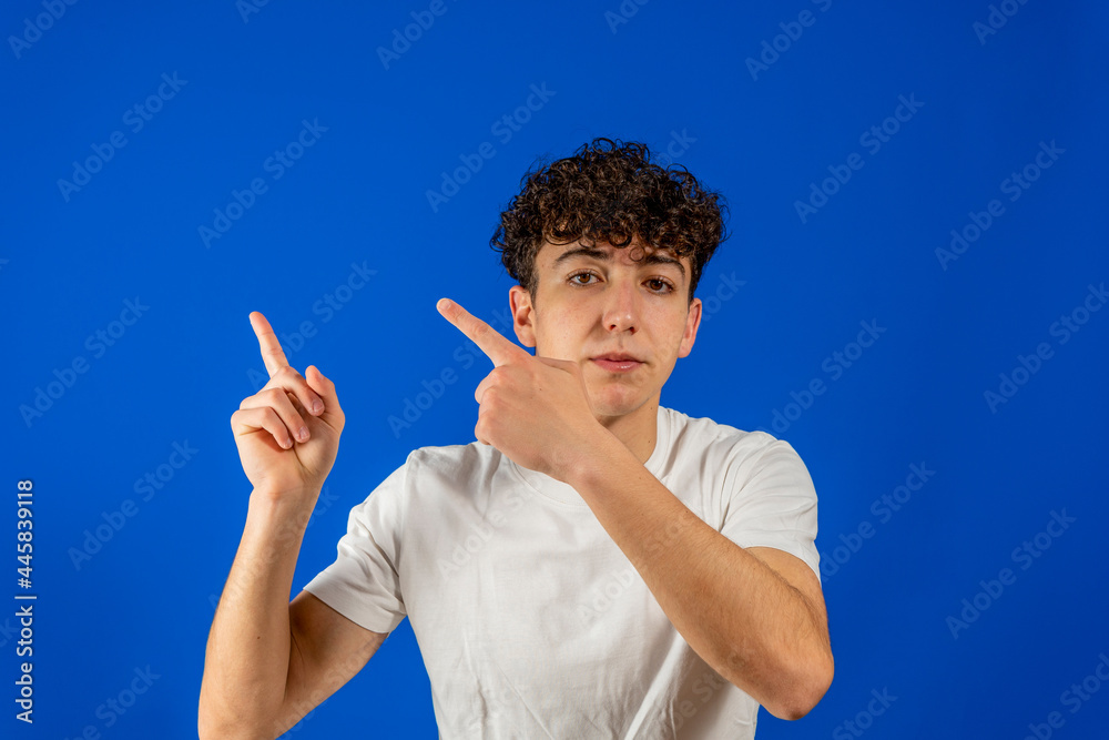 Young man with curly hair pointing towards a corner of the image where the copy space text goes on blue studio background. Marketing concept Young man with curly hair pointing towards a corner of the image where the copy space text goes on blue studio background. Marketing concept
