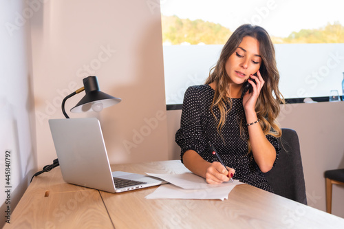 Young Caucasian woman teleworking with a computer at home, making a work call