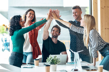 Group of successful smart business team celebrating good job while holding up their right hands on coworking place.