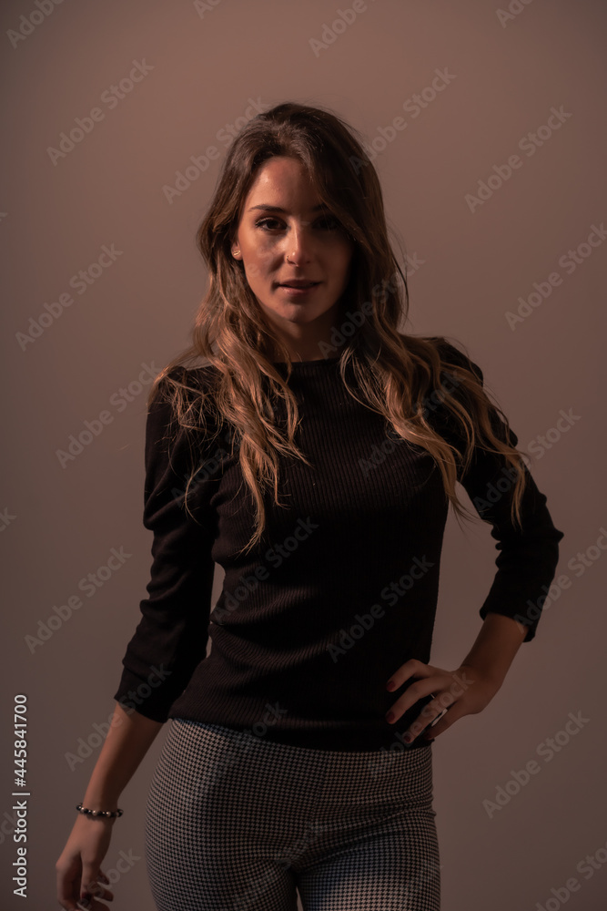 Fototapeta premium Portrait of a young blonde caucasian woman on a brown background with a soft light from the side with looking at camera