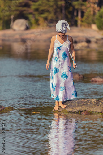 Fototapeta Naklejka Na Ścianę i Meble -  Young woman with a towel on her head at the sea. The lady walks on the water. The concept of summer outdoor recreation, relaxation. good weather